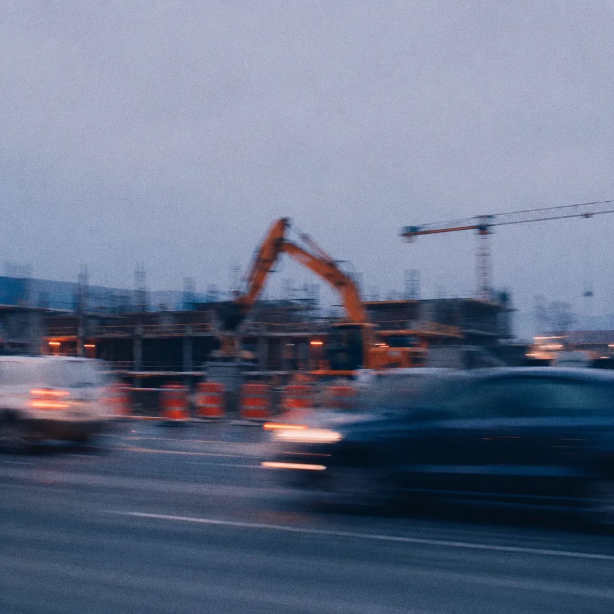 Chantier de construction flou au crépuscule, avec une pelle mécanique et une grue